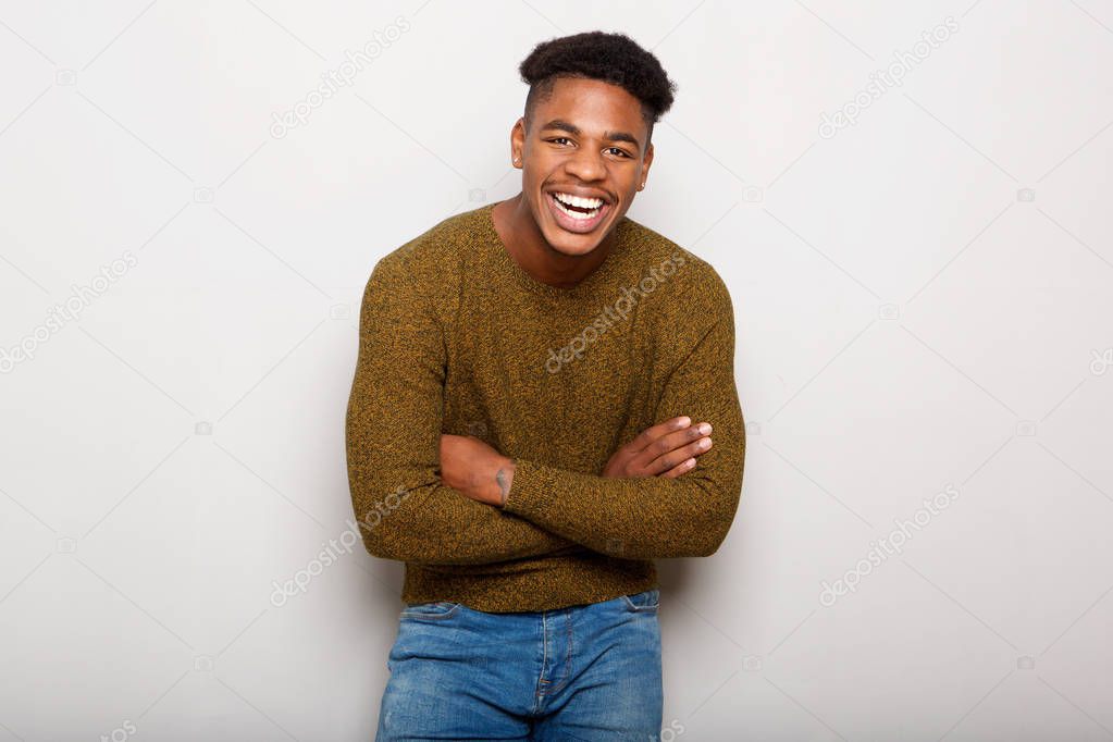 Portrait of cheerful young african american man laughing with arms crossed by gray wall