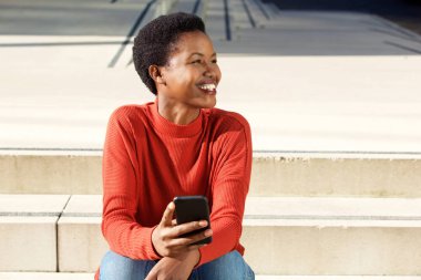 Hareket eden telefon ile dışarıda gülümseyen genç Afro-Amerikan kadın portresi