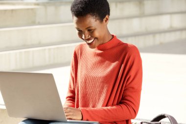 Dizüstü bilgisayarda çalışma dışında oturan genç Afrikalı kadın portresi