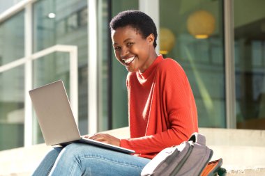 Dizüstü bilgisayarda çalışma dışında oturan neşeli genç kadın portresi yan