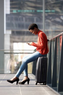 Gülümseyen genç seyahat bavul istasyonunda ve cep telefonu arıyorum oturan tam vücut yan portresi