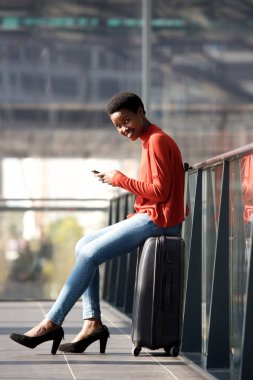 Tam uzunlukta yan portresi genç Afro-Amerikan seyahat çanta ve cep telefonu ile istasyonunda bekleyen kadın