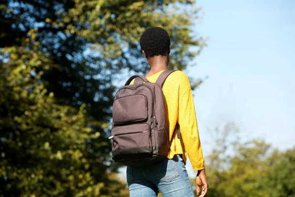 Portrait from behind of young black woman walking in park with bag