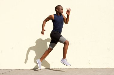 Tam vücut yan duvarın ardında koşan sağlıklı genç siyah adam portresi