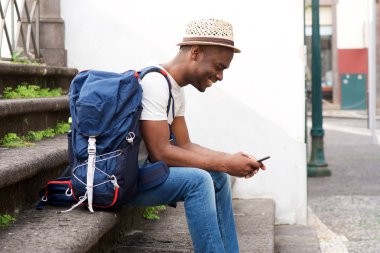Yan çanta ve cep telefonu ile merdivenlerde oturan Afro-Amerikan erkek turist portresi