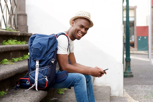バッグと携帯電話を含むステップに座っているアフリカ系アメリカ人男性の観光客の側の肖像 — ストック写真