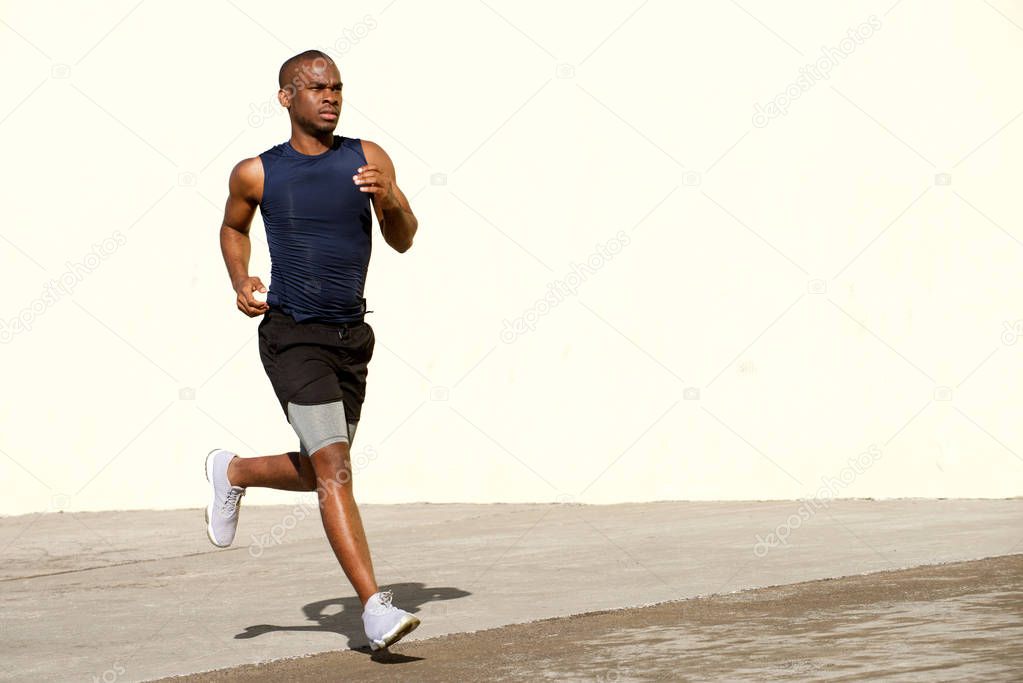 Full body portrait of healthy young black man running outside on street
