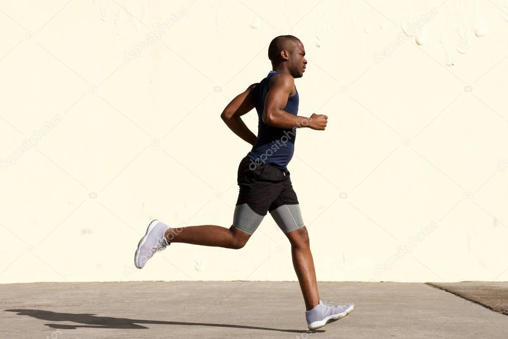 Full body profile portrait of young african american man running by wall
