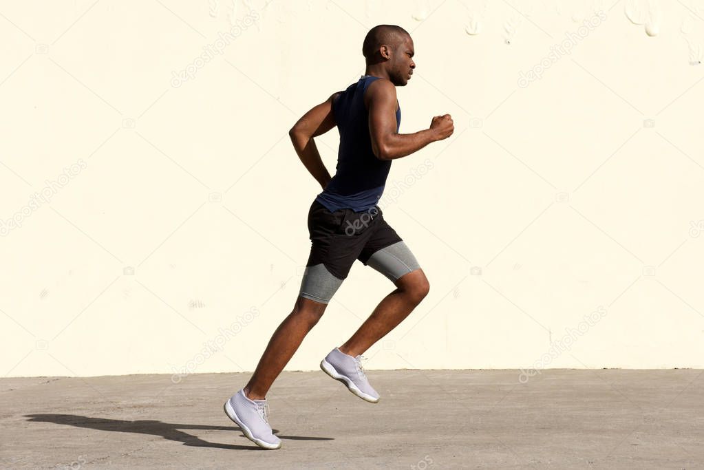 Full body profile portrait of healthy young african american man running by wall