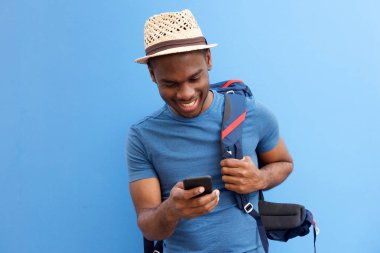 Portrait of cool young african american guy with bag and cellphone against blue background clipart