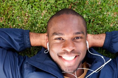 Yukarıdan portresi gülümseyen Afrikalı-Amerikalı adam kulaklık ile müzik dinlemek çim üzerinde yalan