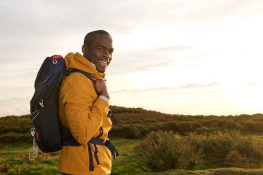 Sırt çantası ayakta açık havada gündoğumu sırasında genç siyah adamla gülümseyen tarafı portresi