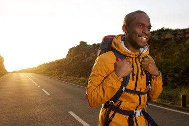 Mutlu genç Afro-Amerikan erkek hiker gündoğumu sırasında yolda yürürken portresi