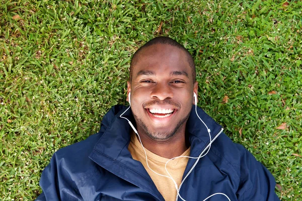 上面的肖像快乐的黑人躺在草地上听着耳机的音乐 — 图库照片