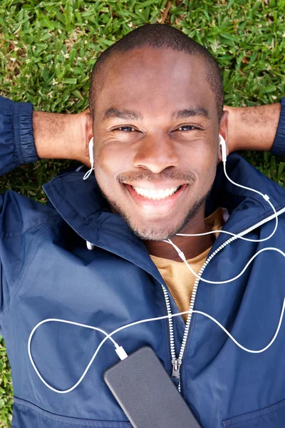 Portrait Smiling Young Black Man Lying Grass Listening Music Earphones — Stock Photo, Image