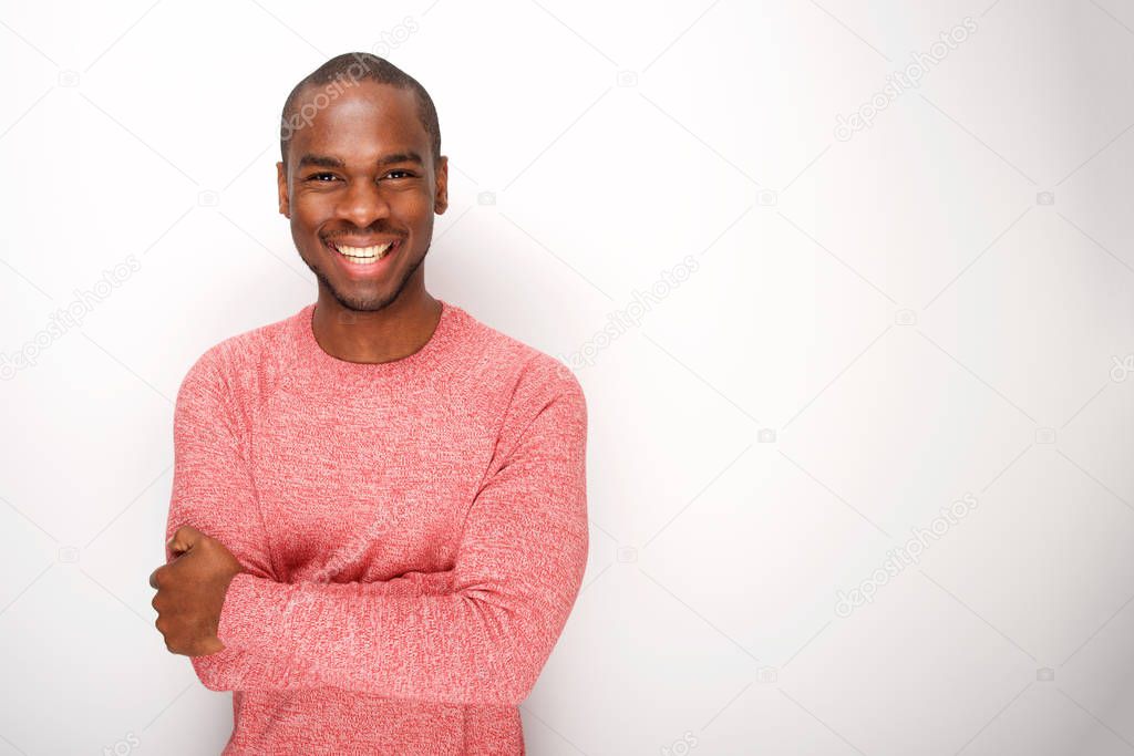Portrait of fashionable young black man smiling with arms crossed by white wall