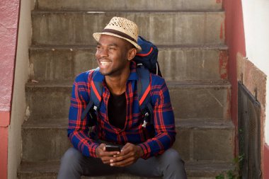 Mutlu Afrika kökenli Amerikalı adam sırt çantası ve cep telefonu ile merdiven üzerinde rahatlatıcı portresi
