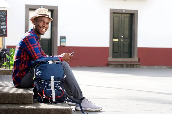 携帯電話とバッグ上の通りリラックスした幸せのアフリカ系アメリカ人旅行男の全身ポートレート — ストック写真