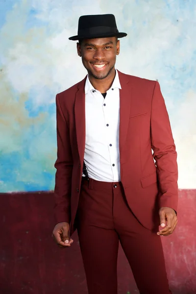 Portrait of handsome black man in vintage suit and hat smiling by wall