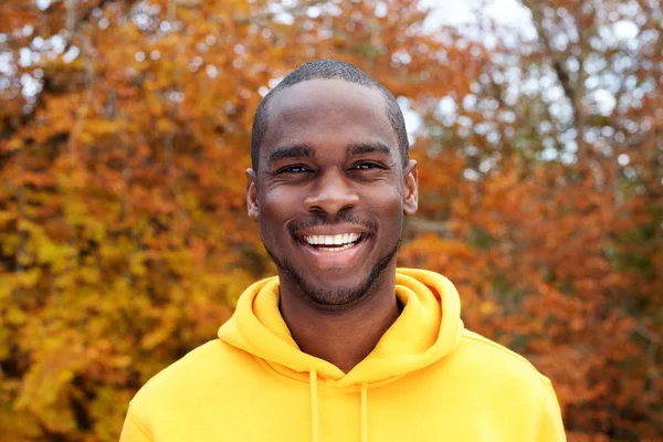 背景に秋の葉に対して微笑むハンサムな若い黒人男性のポートレートをクローズアップ — ストック写真