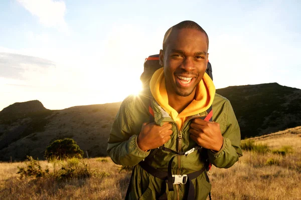 背景にバックパックと夕日と山でハイキング幸せなアフリカ系アメリカ人男性の肖像 — ストック写真
