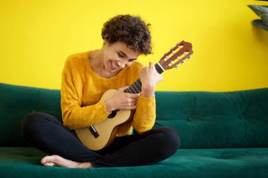 Gitar enstrümanı ile kanepede oturan mutlu genç Afrikalı-Amerikalı kadın portresi