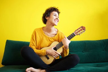 Gitar ile kanepede oturan genç mutlu afro-amerikan kadın portresi