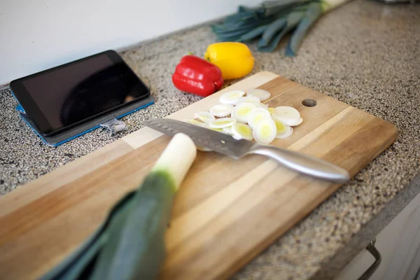 Chopping board with knife and vegetables on kitchen counter with digital tablet