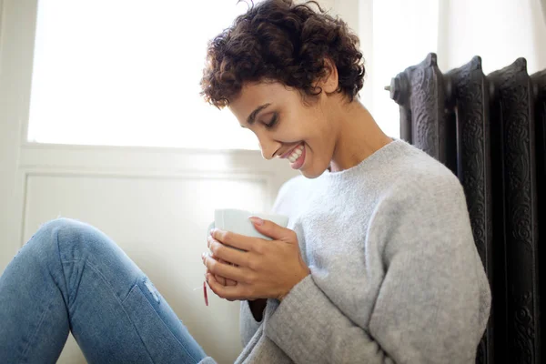 お茶のカップでラジエーターヒーターに対して床に座ってリラックスした若い女性の肖像画 — ストック写真