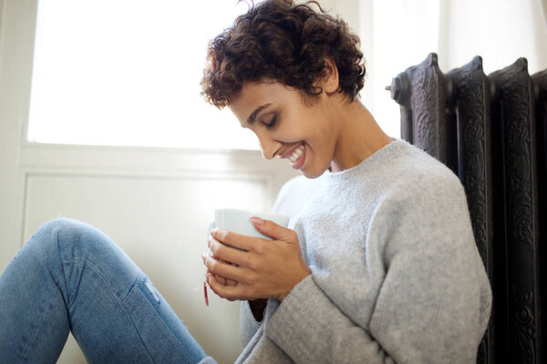 Portrait of relaxed young woman sitting on floor against radiator heater with cup of tea