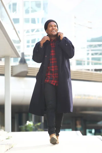 街で冬のジャケットとビーニーで歩く幸せなアフリカ系アメリカ人のフルボディの肖像画 — ストック写真