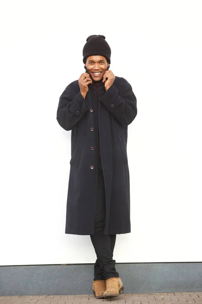 Full body portrait of african american male fashion model smiling with winter jacket and beaning by white wall