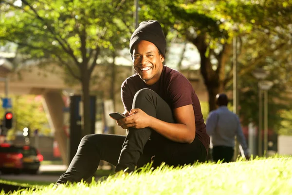Portret Szczęśliwego Przystojnego Młodego Czarnego Mężczyzny Siedzącego Parku Telefonem Komórkowym — Zdjęcie stockowe