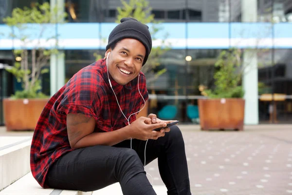 携帯電話とヘッドフォンで街に座っているクールな若いアフリカ系アメリカ人男性の肖像画 — ストック写真