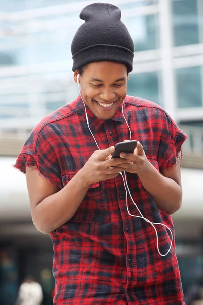 街で携帯電話とイヤホンで音楽を聴いている笑顔のアフリカ系アメリカ人男性の肖像 — ストック写真