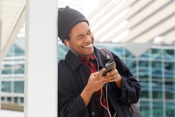 街で笑う携帯電話とイヤホンを持つ幸せなアフリカ系アメリカ人男性の肖像画 — ストック写真