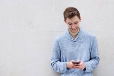 Duvardan akıllı telefon bakarak gülümseyen genç adam portresi