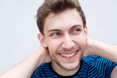 Beyaz duvar la başının arkasında elleri ile gülümseyen yakışıklı genç adamın yakın portresi