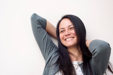 Beyaz arka plana karşı baş arkasında elleri ile neşeli Genç Asyalı kadın portre yakın 