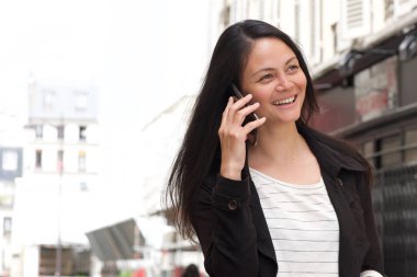 Şehirde cep telefonu ile konuşan mutlu genç kadının portresi