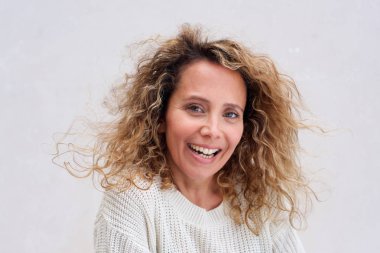 Beyaz arka plana karşı kıvırcık saçlı gülümseyen mutlu orta yaş kadının portre yakın