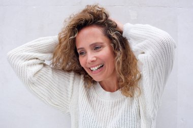 Beyaz duvara karşı baş arkasında elleri ile neşeli orta yaş kadın portre yakın