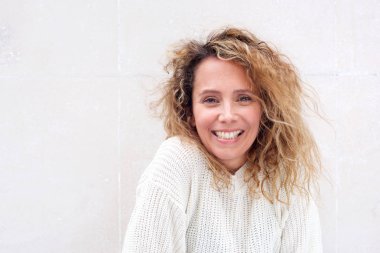 Beyaz arka plana karşı kıvırcık saçlı gülümseyen orta yaş kadın portre yakın 