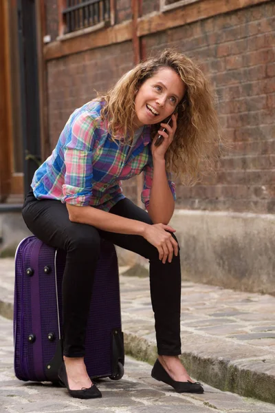 スーツケースに座って街の通りで携帯電話と話す旅行女性の肖像画 — ストック写真