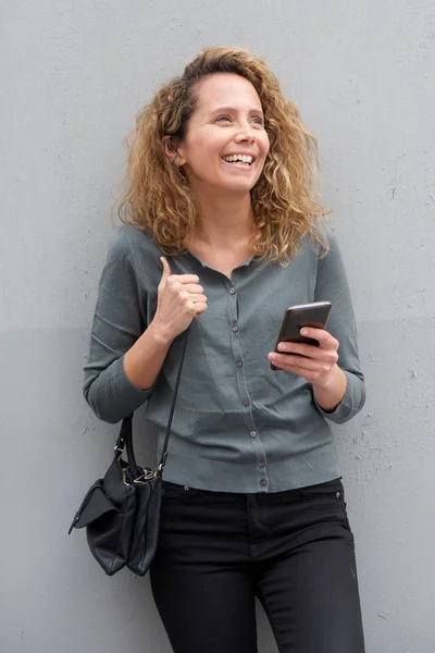 Portret Uśmiechniętej Atrakcyjnej Kobiety Kręconymi Włosami Telefonem Komórkowym Przez Szarą — Zdjęcie stockowe