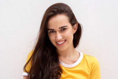 Beyaz duvara karşı gülümseyen genç esmer kadının ön portresini kapatın