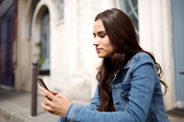 Şehirde cep telefonu bakarak güzel genç kadının yan portre
