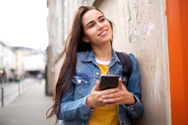 Şehirde cep telefonu tutan kahverengi saçlı mutlu genç kadın portresi