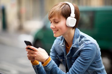 Cep telefonu ve kulaklıkla gülümseyen genç kadının portresini kapatın