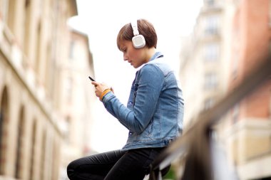Side portrait of young woman looking at mobile phone while listening to music with headphones